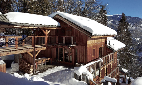 Traditional wooden ski chalet in Méribel, France, with snow-covered roofs, balconies and surrounding Alpine scenery.