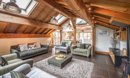 Spacious Méribel ski chalet living room with exposed wooden beams, comfortable sofas, armchairs and a log-burning stove.